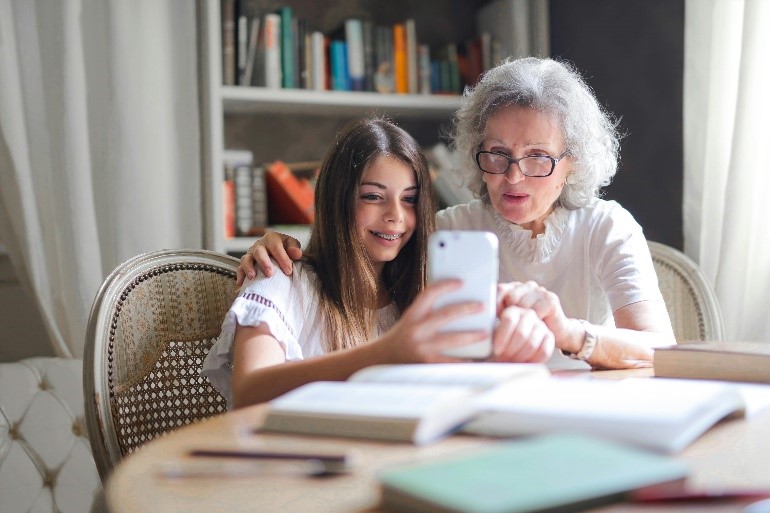 A n older woman and pre-teen smile while using a smartphone.