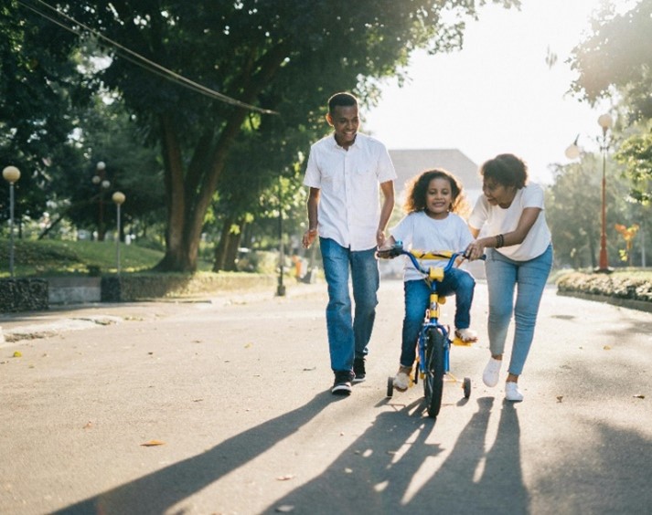 A mother and father help their child ride a bicycle outside