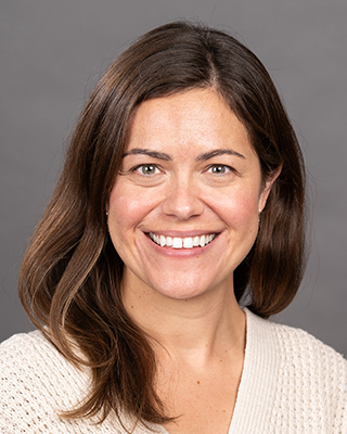 A smiling white woman with brown hair in an off-white top against a grey background